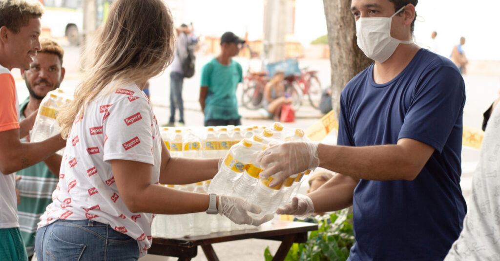 Two people wearing mask and gloves while giving out food and water to people in need during COVID