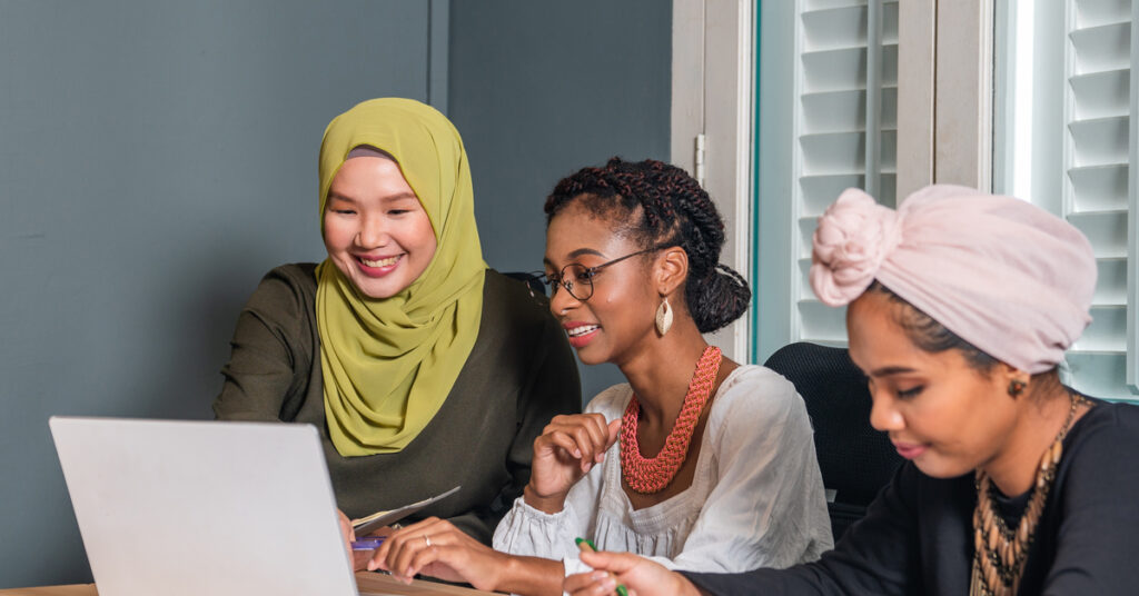 three diverse women siting down at table looking at a laptop